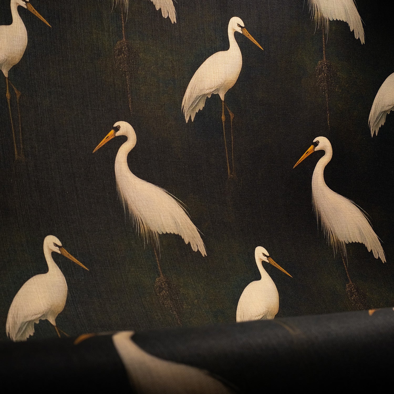 White heron patterned upholstery fabric styled in a moody green interior with soft lighting.