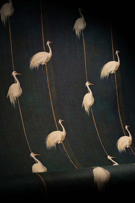 Linen blend upholstery fabric featuring cranes perched on golden reeds against a moody green backdrop, styled as curtain drape.