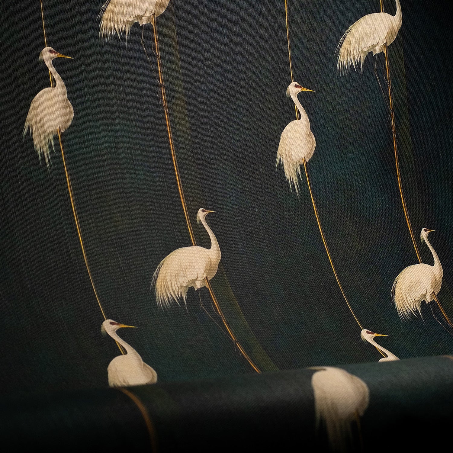 Linen blend upholstery fabric featuring cranes perched on golden reeds against a moody green backdrop, styled as curtain drape.