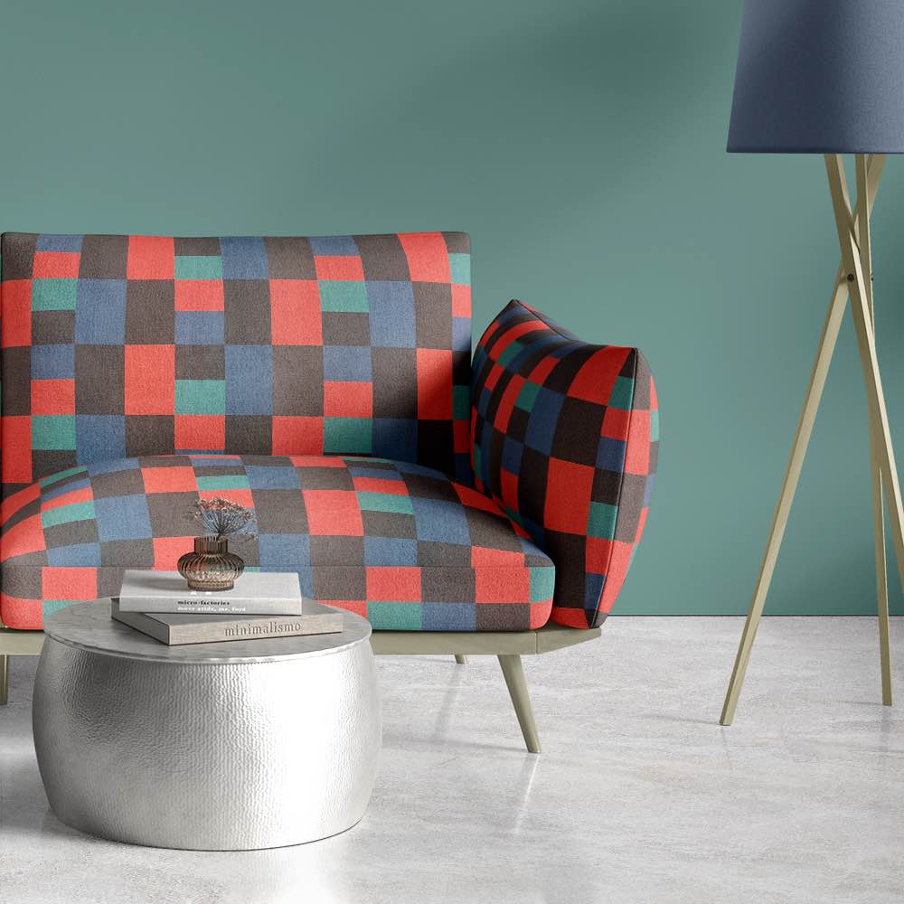 Modern armchair upholstered in Cubism No.20 bold geometric red, blue, and teal upholstery fabric against soft green wall