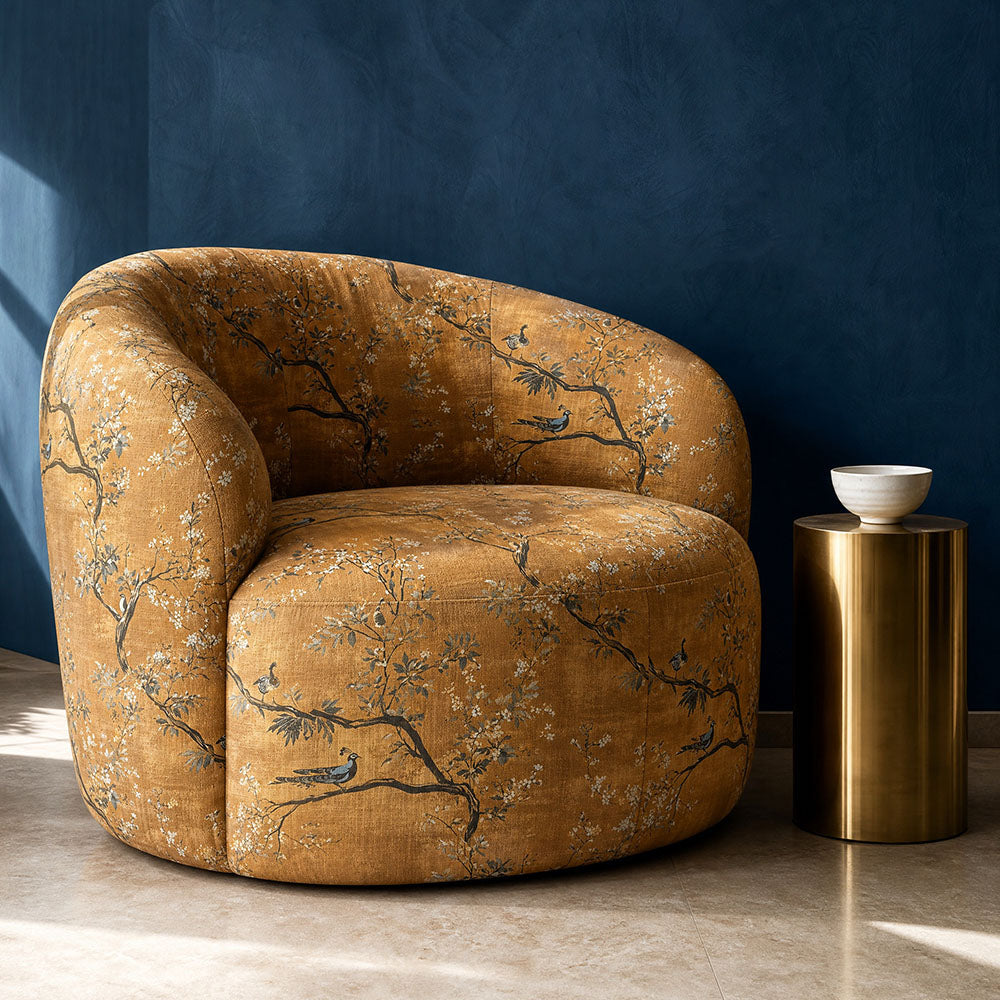 Pavone upholstery fabric featuring elegant peacocks perched amongst blossoming branches in rich ochre, sage green and ivory tones upholstered onto a contemporary curved accent chair