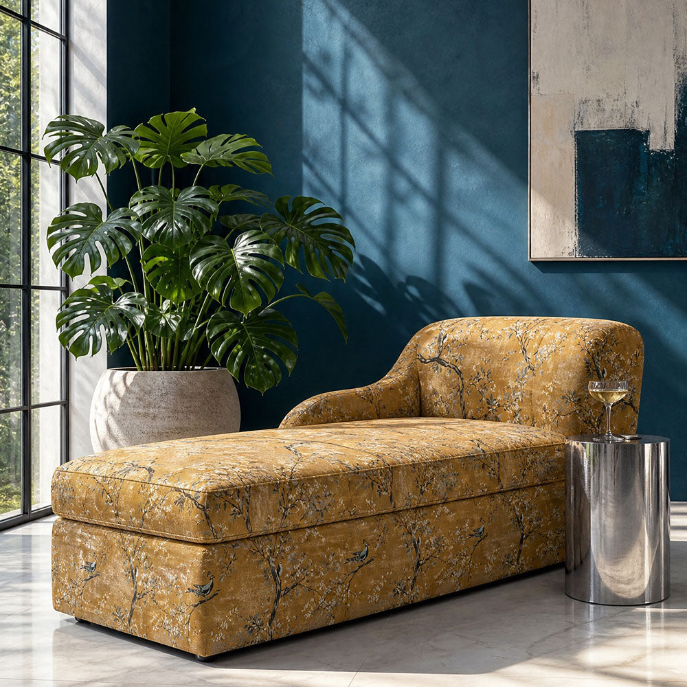 Luxury upholstery fabric with decorative peacock and flowering branch design in warm ochre and muted botanical tones upholstered onto a contemporary chaise longue