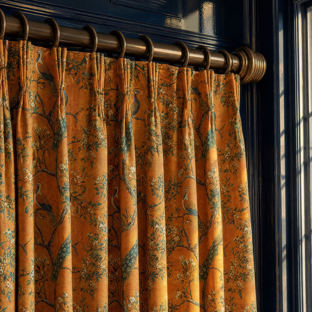 Peacock curtain fabric featuring detailed peacock motifs, flowering branches and botanical foliage in rich ochre, teal and sage green tones styled as elegant full-length curtains