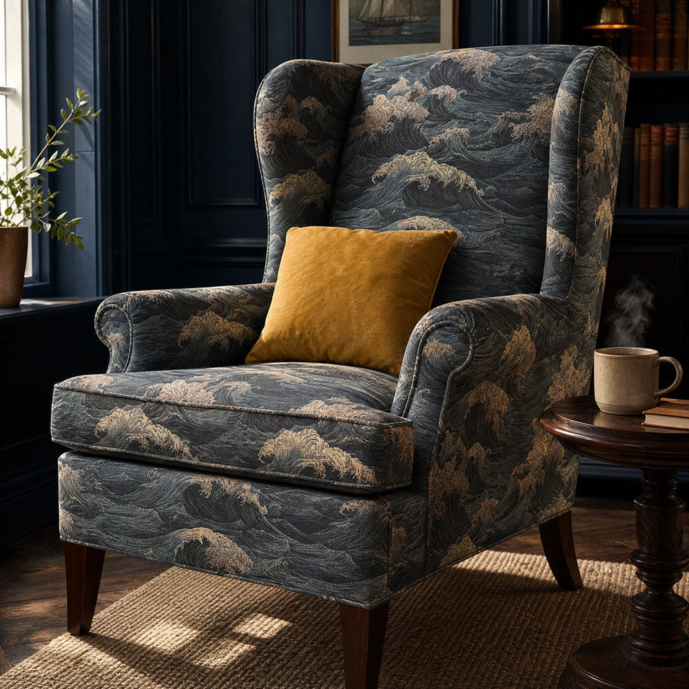 Waves upholstery fabric featuring dramatic ocean wave motifs inspired by traditional Japanese seascapes in deep navy blue, charcoal and soft gold tones upholstered onto a wingback armchair