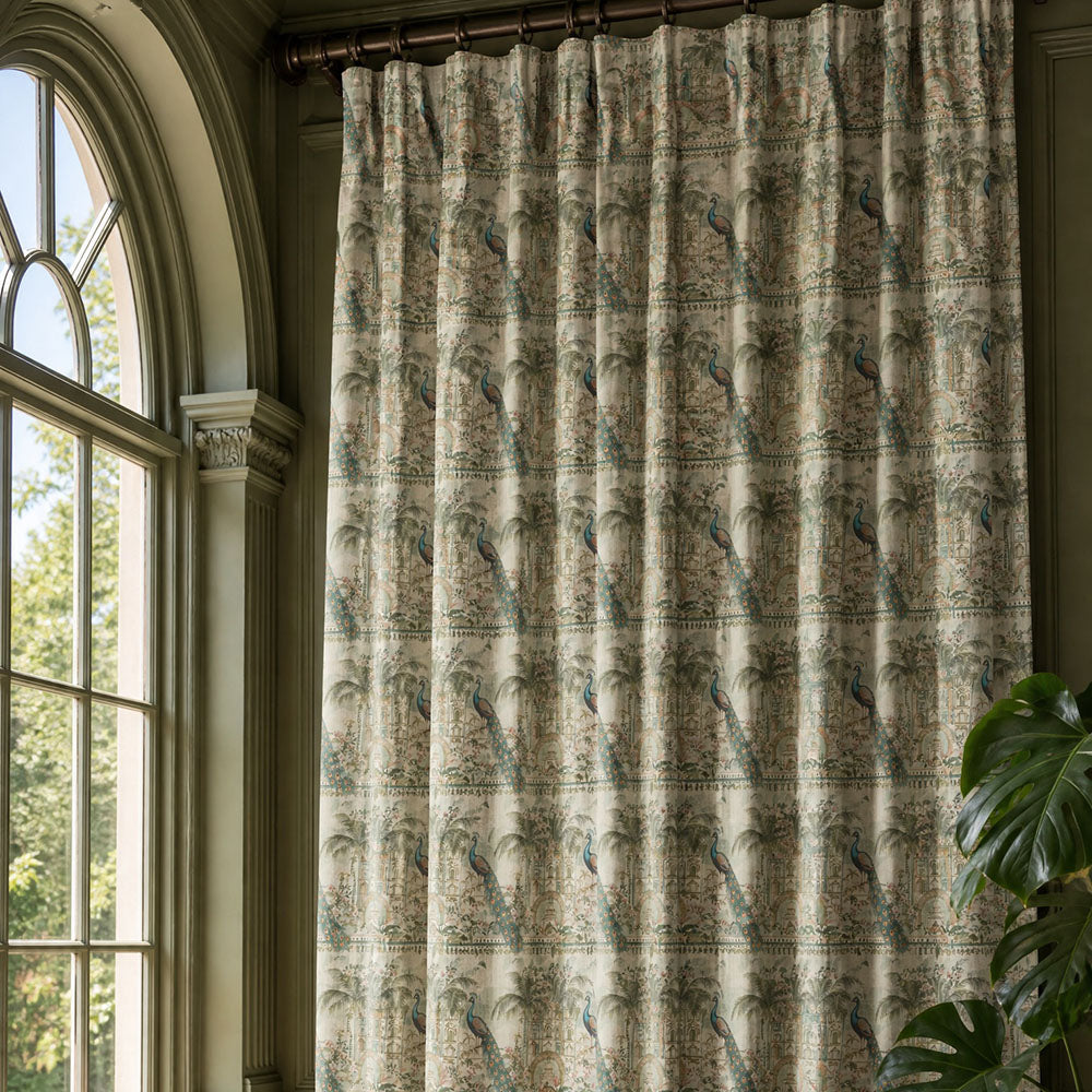 Agra curtain fabric featuring intricate peacock motifs, tropical palms and decorative architectural detailing in soft sage green, teal and natural tones styled as luxury pencil pleat curtains