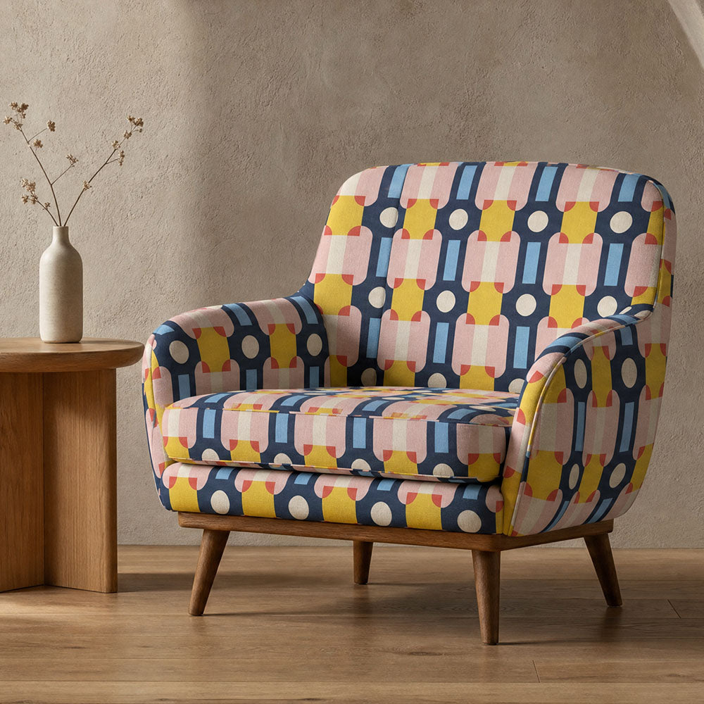 Bauhaus inspired upholstery fabric featuring bold geometric shapes, circular motifs and architectural forms in navy blue, blush pink, ochre and ivory tones upholstered onto a contemporary armchair